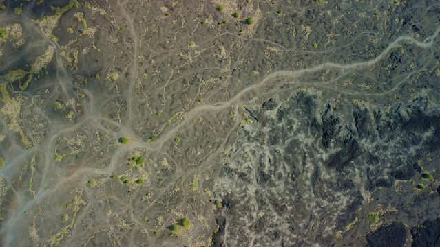 Top down shot of the surface texture of volcanic soil near the volcano. Trails from hiking trails on black lava, sun glare and green hills. Background video with beautiful nature.