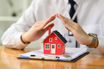 Man hands protecting over little house. Property insurance, security and real estate concept