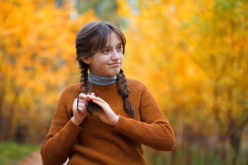 a young teenage girl poses in an autumn forest, enjoying the beautiful nature and bright yellow leaves