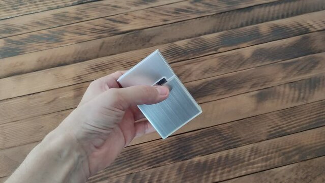 Man twists a metal cigarette case in left hand on a wooden background