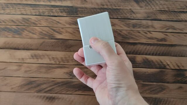 Man twists a metal cigarette case in right hand on a wooden background