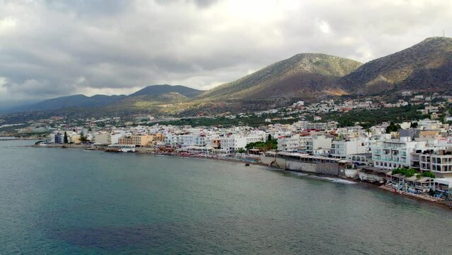 Slow-motion aerial view of the seaside in the city of Hersonissos on the Greek island of Crete. The drone flies over the sea towards the city.
