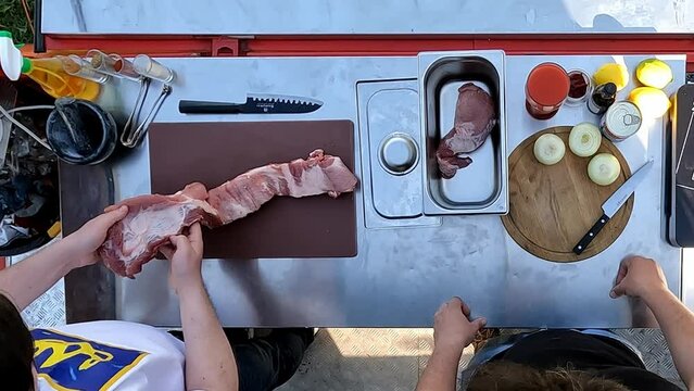 Top view image of two men standing at table in garden and starting cooking meat. Fresh pork with vegetables. Concept of food, cuisine, hobby, taste, weekend activity, street cookery
