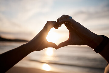 Couple, heart and hands at beach in sunset for love, care and relax on holiday, vacation and travel. Closeup of people, silhouette and finger shape at sea for support, freedom and emoji sign in sky