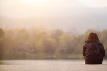 young woman sits on walkway by reservoir watching beautiful scenery of reservoir alone in the evening. back of woman sitting by reservoir alone in evening and with copy space for text.