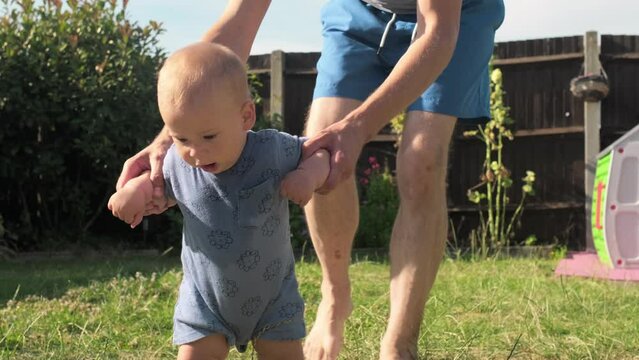 baby takes first steps in grass. Dady Father walks with son in nature kid dream concept. baby takes first steps with mom. mom and little son feet baby close-up happy family Hot Summer Day. Fatherhood