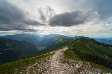 The road through the Tatra mountains in summer, the sky is covered with clouds, the rays of the sun break through the clouds. © Dmitri