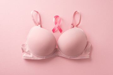 Symbolic breast cancer awareness. Pink-themed top view photo featuring a bra and pink ribbon on a pastel pink surface. Space available for text or advert placement - obrazy, fototapety, plakaty