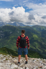 Fototapeta premium Male traveler with a briefcase behind his back in the Tatra Mountains in summer, view from the back.