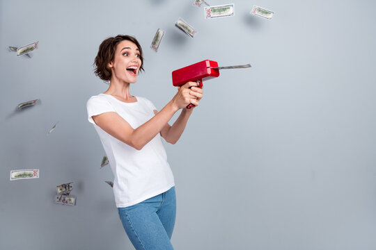 Photo of lucky excited woman dressed white t-shirt shooting money gun empty space isolated grey color background