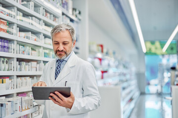 A male pharmacist holding a digital tablet and using it for medical inventory.