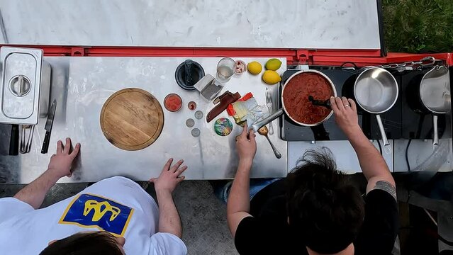 Top view image. Two men cooking outdoors, preparing tomato sauce for meat. Outdoor kitchen. Adding soy sauce. Concept of food, cuisine, hobby, taste, weekend activity, street cookery