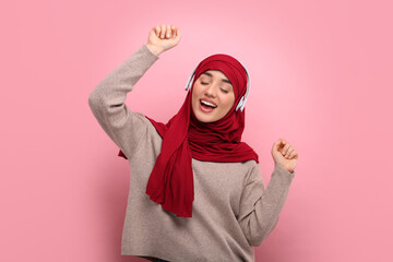 Muslim woman in hijab and headphones dancing on pink background