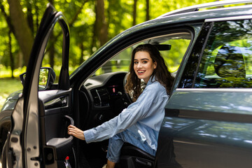 Portrait of gorgeous brunette in shirt entering her car. With one hand woman is shutting door.
