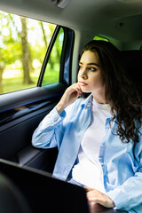 Businesswoman working on laptop and talking on phone while travelling in a taxi.