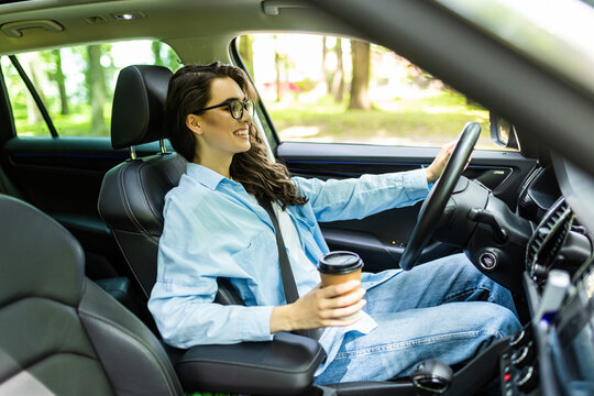 Happy Young Woman With Coffee To Go Driving Her Car. Woman Sipping A Coffee While Driving A Car.