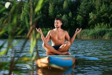 Man meditating on color SUP board on river