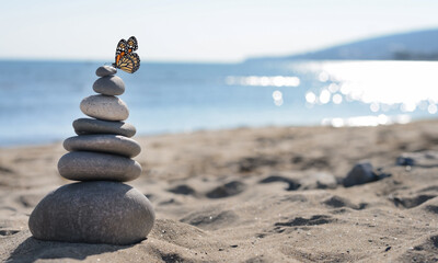 Peace and harmony. Stacked pebbles on sand and beautiful butterfly near sea. Banner design with space for text