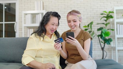 Elderly Asian mother and young daughter enjoy shopping online on smartphone at home. Daughter and mother using smartphone and holding credit card while shopping online