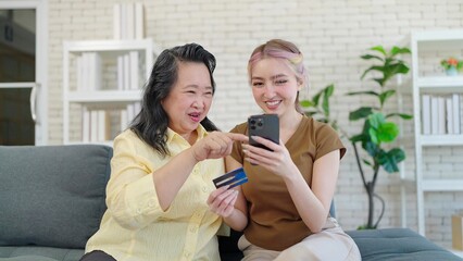 Elderly Asian mother and young daughter enjoy shopping online on smartphone at home. Daughter and mother using smartphone and holding credit card while shopping online
