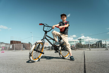 A boy in a cap and T-shirt rides a bmx bike and learns to perform tricks near a special ramp for...