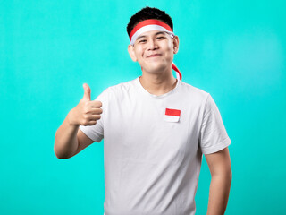 A portrait of an Asian man celebrating Independence Day, wearing a white shirt with a red and white headband, making an OK pose with his thumb up, isolated with a turquoise background.