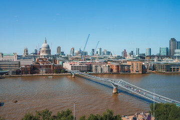 Fototapeta premium Millennium bridge over river Thames. Financial district with clear sky in background. Buildings in city during sunny day at London.