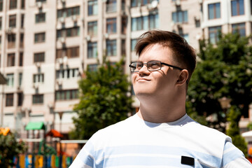 A smiling young man with Down syndrome in glasses poses against the background of the city in the...