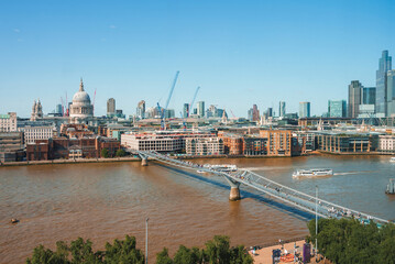 Fototapeta na wymiar Millennium bridge over river Thames on sunny day. Financial district with clear sky in background. Buildings in city at London.