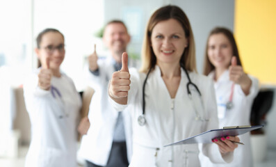 Fototapeta na wymiar Successful medical team in white coats hold their thumbs up. Medical services concept