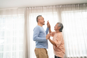 Romantic and cheerful Asian well-being senior couple enjoy dancing and holding hands to music together with smiles and happiness in the living room. Senior retirement activity at home.