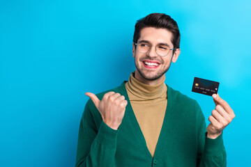 Photo of cute dreamy guy dressed green cardigan eyewear showing thumb empty space holding credit...