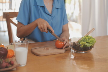 A young woman with a beautiful face in a blue shirt with long hair eating fruit sitting inside the kitchen at home with a laptop and notebook for relaxation, Concept Vacation.