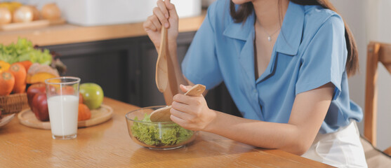 A young woman with a beautiful face in a blue shirt with long hair eating fruit sitting inside the kitchen at home with a laptop and notebook for relaxation, Concept Vacation.