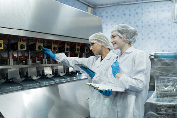 Two female worker inspecting quality of plastic water tank on conveyor belt in drinking water...