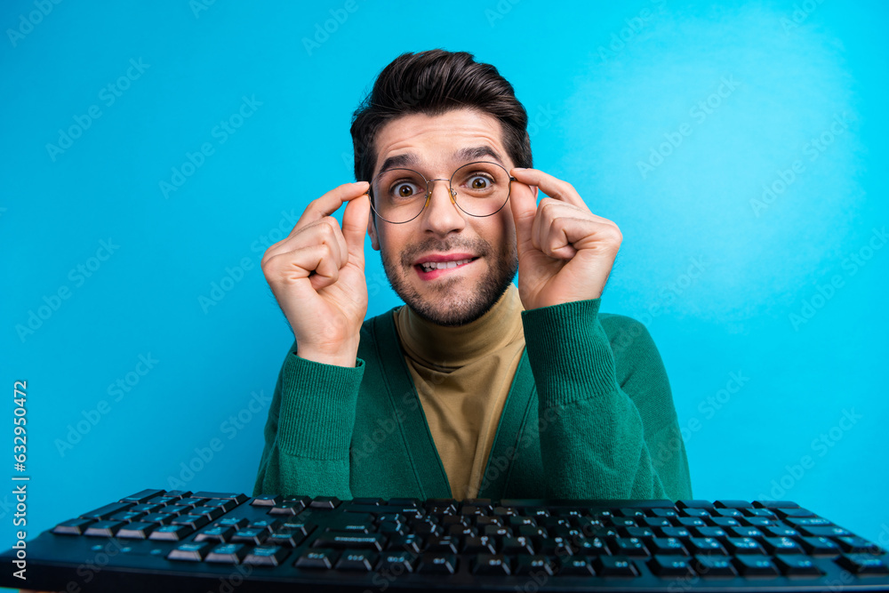 Poster Photo of young nervous man nerd biting lips near computer keyboard wish get invite from best university isolated on blue color background