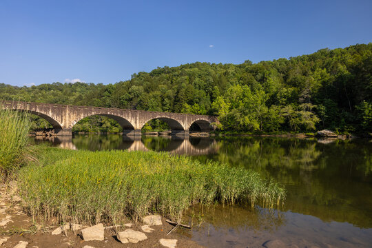 A bridge with arches crossing a calm river during summer.