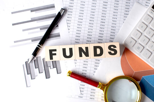 FUNDS text on wooden block on graph background with pen and magnifier