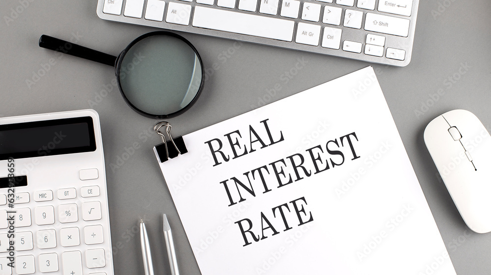 Aufkleber real interest rate written on paper with office tools and keyboard on the grey background