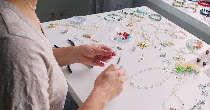 Female jewelry designer working in studio making necklace and earrings