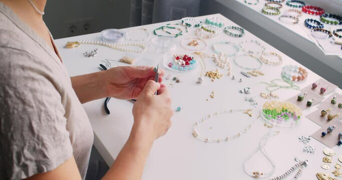 Female jewelry designer working in studio making necklace and earrings