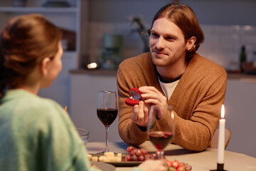 Portrait of young man holding open box with engagement ring while proposing to girlfriend at dinner