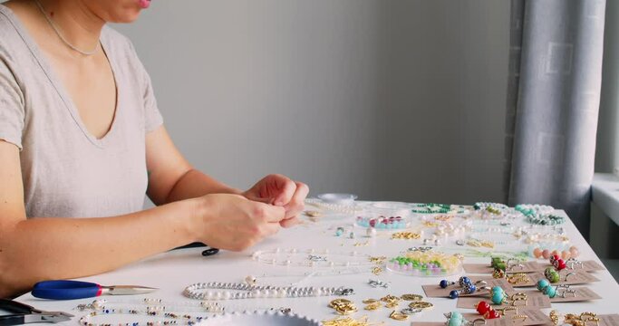 Female jewelry designer working in studio making necklace and earrings