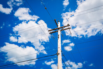 Electricity pole and power lines against the blue sky with white clouds. Summer forest landscape in...