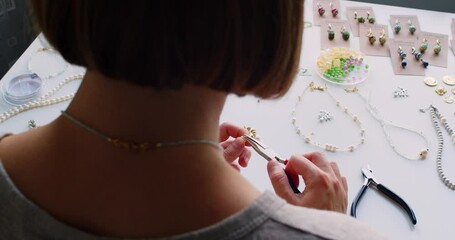 Female jewelry designer working in studio making necklace and earrings