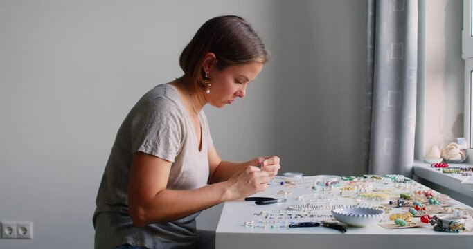 Female jewelry designer working in studio making necklace and earrings