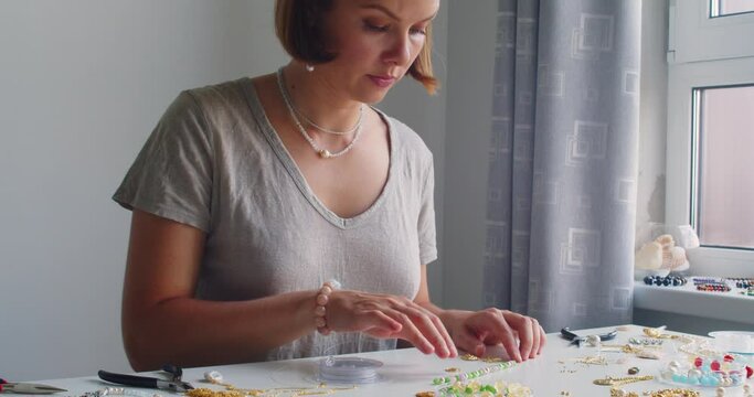 Female jewelry designer working in studio making necklace and earrings