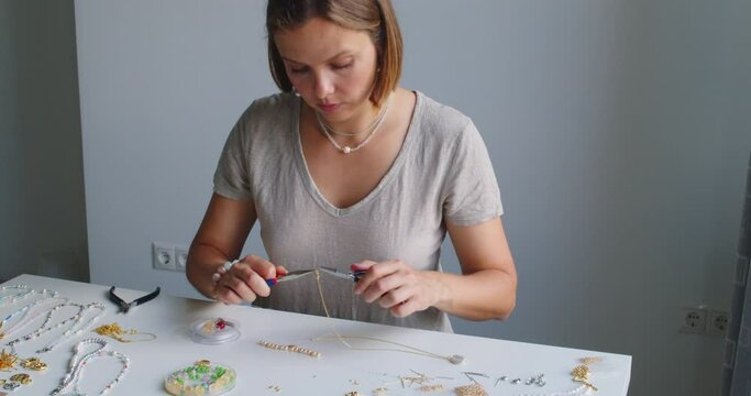 Female jewelry designer working in studio making necklace and earrings