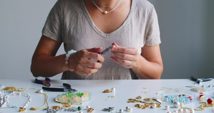 Female jewelry designer working in studio making necklace and earrings