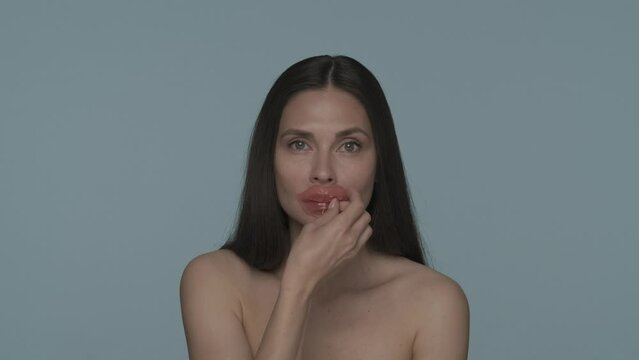 Portrait of a seminude woman with hyaluronic patches on her lips in the studio on a blue background close up. The woman removes the patches and sends an air kiss. HDR BT2020 HLG Material.